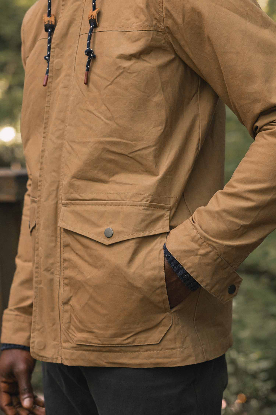 Marshall Jacket in Dark Khaki waxed canvas, a tan hooded utility jacket featuring two large flap pockets and drawstrings at the neck.