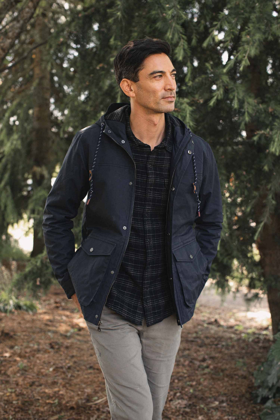 A man wears a navy Bridge & Burn Marshall Jacket / Navy Waxed Canvas with a front zipper and snap-button pockets over a dark plaid shirt.