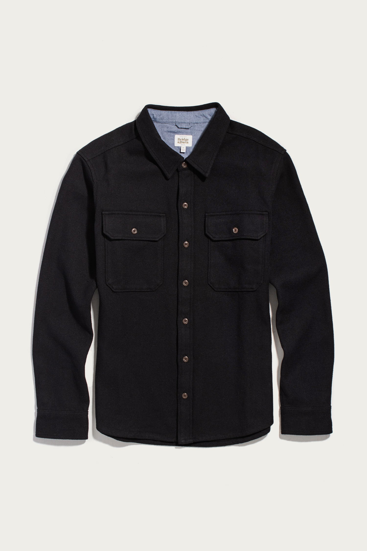 The Bridge & Burn Pointer Overshirt in Ink Stone is a long-sleeve black twill overshirt, featuring two chest pockets and a pointed collar. Crafted from recycled fibers and photographed laid flat on a plain white background, this piece offers a stylish and sustainable choice for your wardrobe.