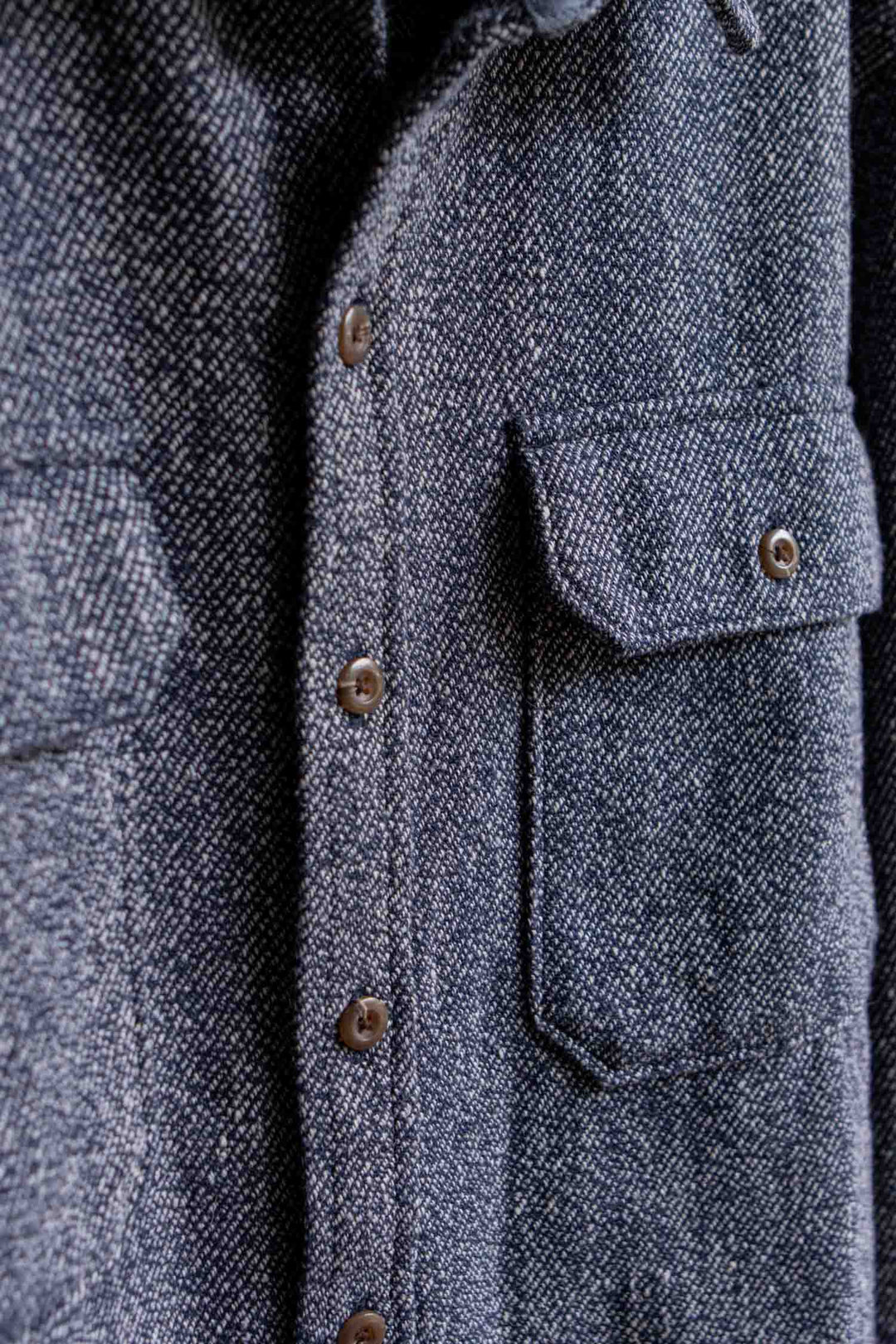 Close-up of the Pointer Overshirt in Ocean Marl by Bridge & Burn, showcasing its textured dark gray twill weave, brown buttons, and flap pockets. Crafted from recycled fibers, this piece highlights meticulous stitching and fabric details, reflecting Bridge & Burn’s commitment to sustainable style.