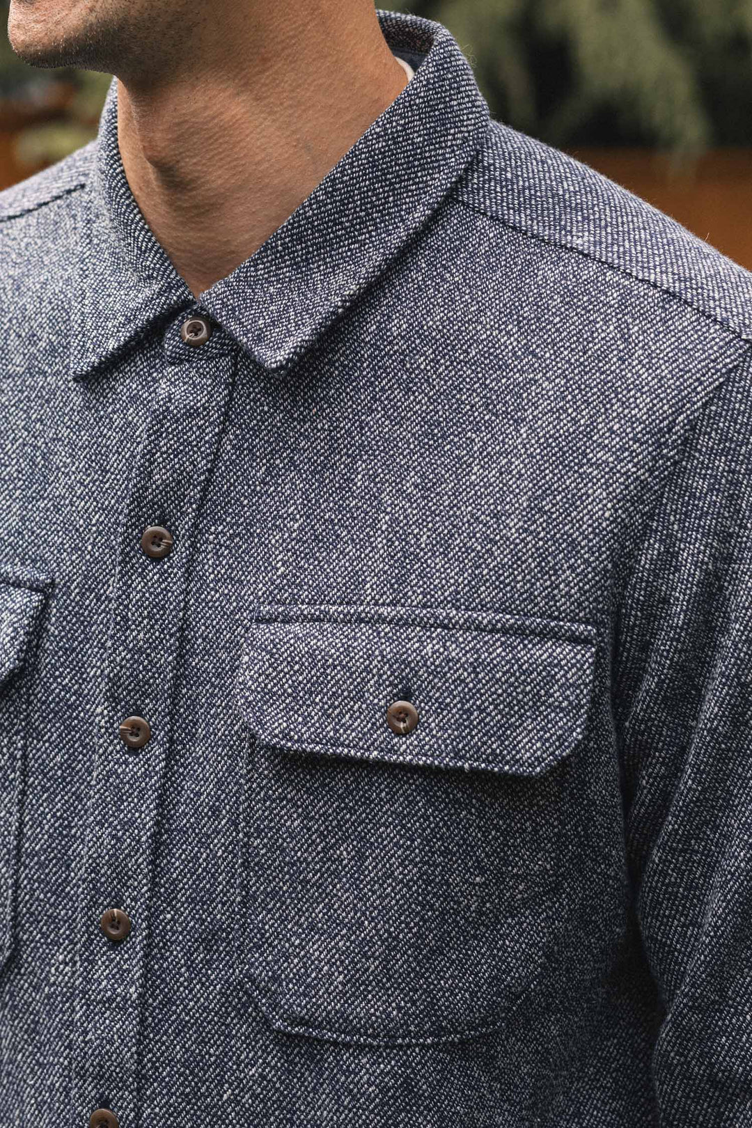 Close-up of a person wearing the Pointer Overshirt in Ocean Marl by Bridge & Burn, featuring a textured blue twill fabric, two chest pockets, and brown buttons. The shot focuses on this sustainably crafted piece made from recycled fibers.