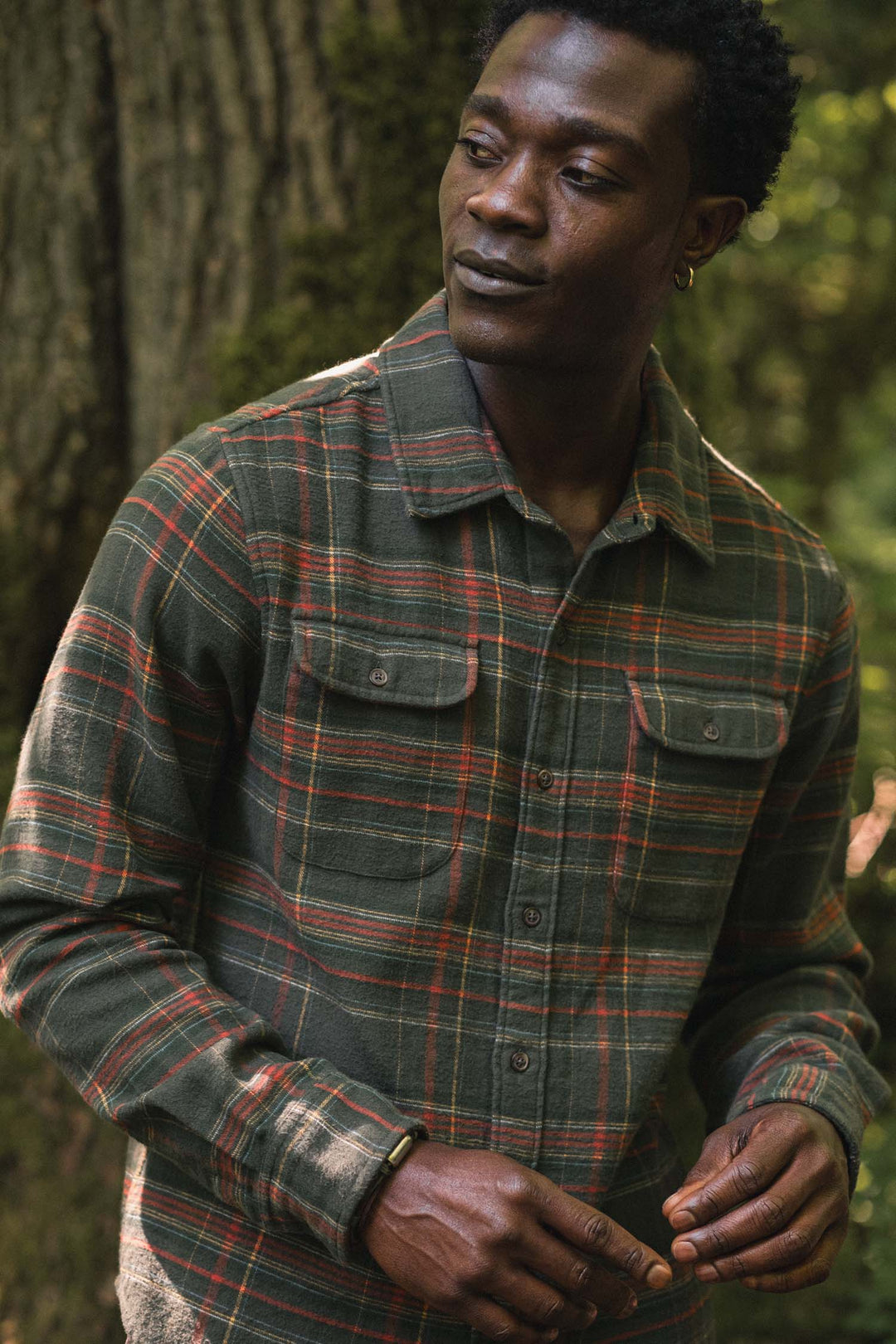 A man wears a Bridge & Burn Cole Slim Shirt in Timberline Plaid, a slim-fit, long-sleeve dark green button-down with two chest pockets.
