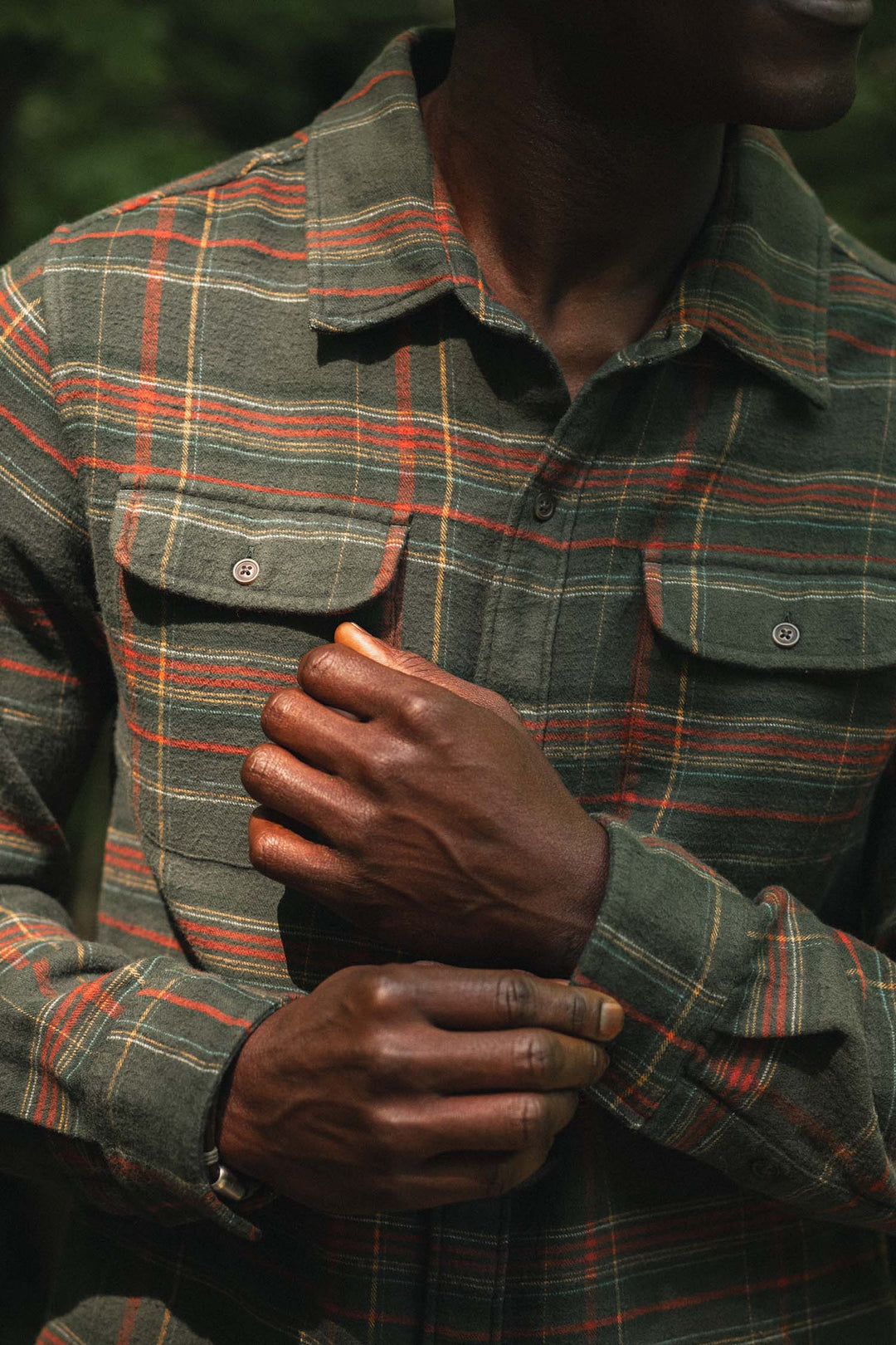 Person wearing a Bridge & Burn Cole Slim Shirt in Timberline Plaid, a slim-fit, long-sleeved green plaid button-down shirt with two button-flap chest pockets.