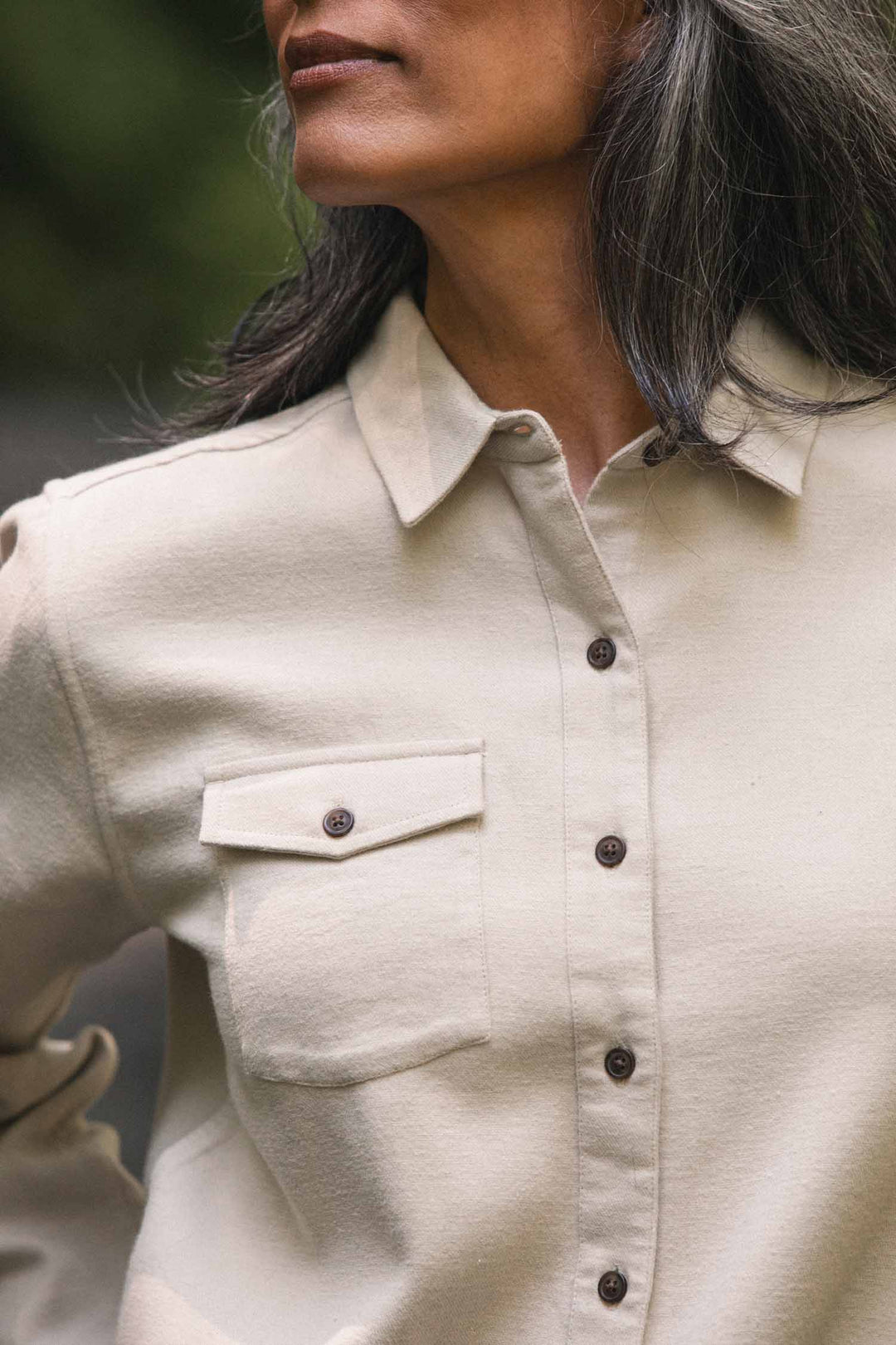 A person with long, gray hair wears the Bridge & Burn Bird Shirt in Fawn Flannel—a relaxed-fit, beige button-up with a front pocket, crafted from organic cotton—outdoors in natural light.