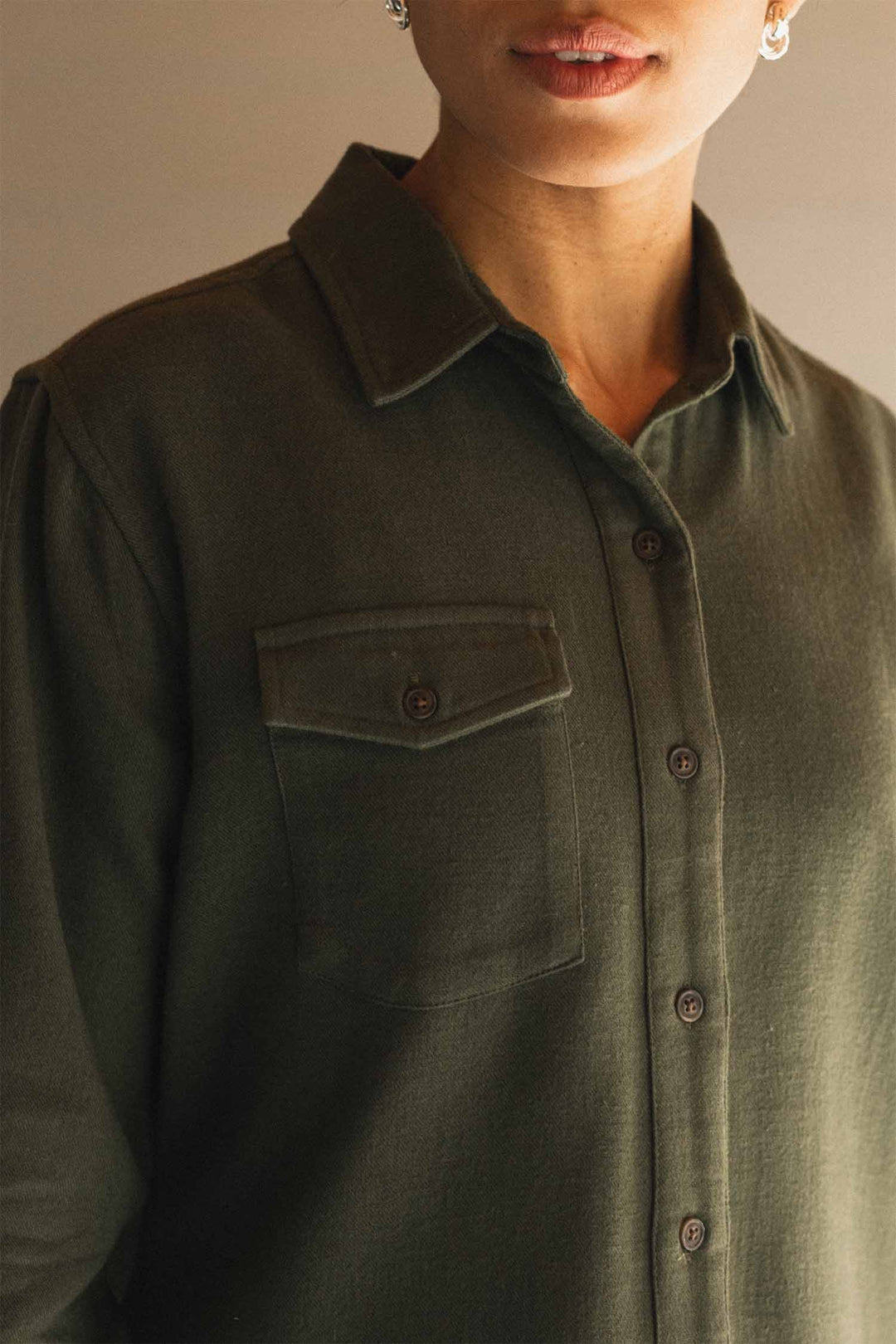 A person wearing the Bridge & Burn Bird Shirt in Pine Flannel—an organic cotton button-up with a chest pocket and collar—shown from the shoulders to the mouth in soft lighting.