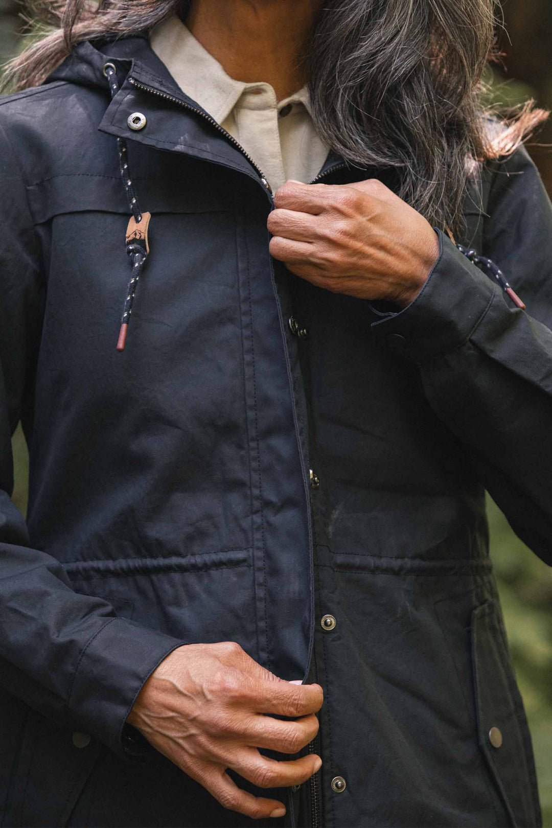 A person wearing a navy blue Bridge & Burn Briar Jacket, a waxed canvas hooded parka with a buttoned placket and drawstring hood.