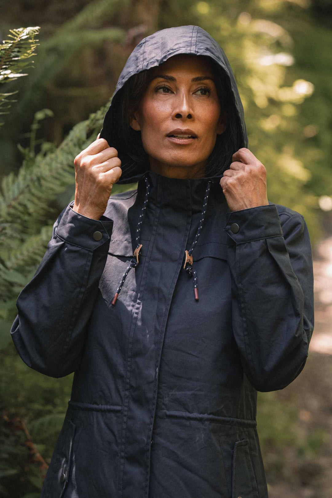 A person pulling the hood of their navy Briar Jacket / Navy Waxed Canvas parka up over their head.
