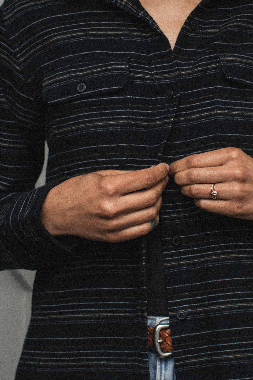 Person buttoning a relaxed fit BCI cotton Lenon Shirt in Raven Stripe with thin horizontal white stripes.
