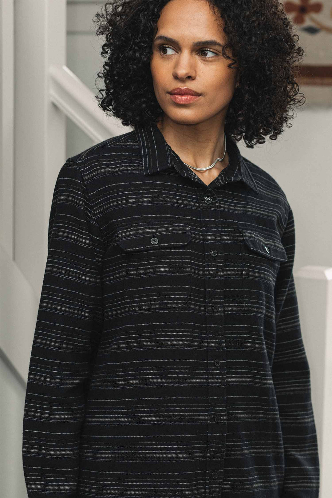 A person wearing a black Bridge & Burn Lenon Shirt / Raven Stripe featuring thin horizontal white stripes, a relaxed fit, and two chest pockets.