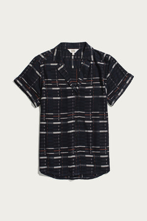 The Bridge & Burn Innes Shirt in Nightfall Stripe is a short-sleeve, relaxed fit button-up crafted from eco-friendly viscose, featuring a dark blue base with white, gray, and red plaid pattern, displayed laid flat on a white background.