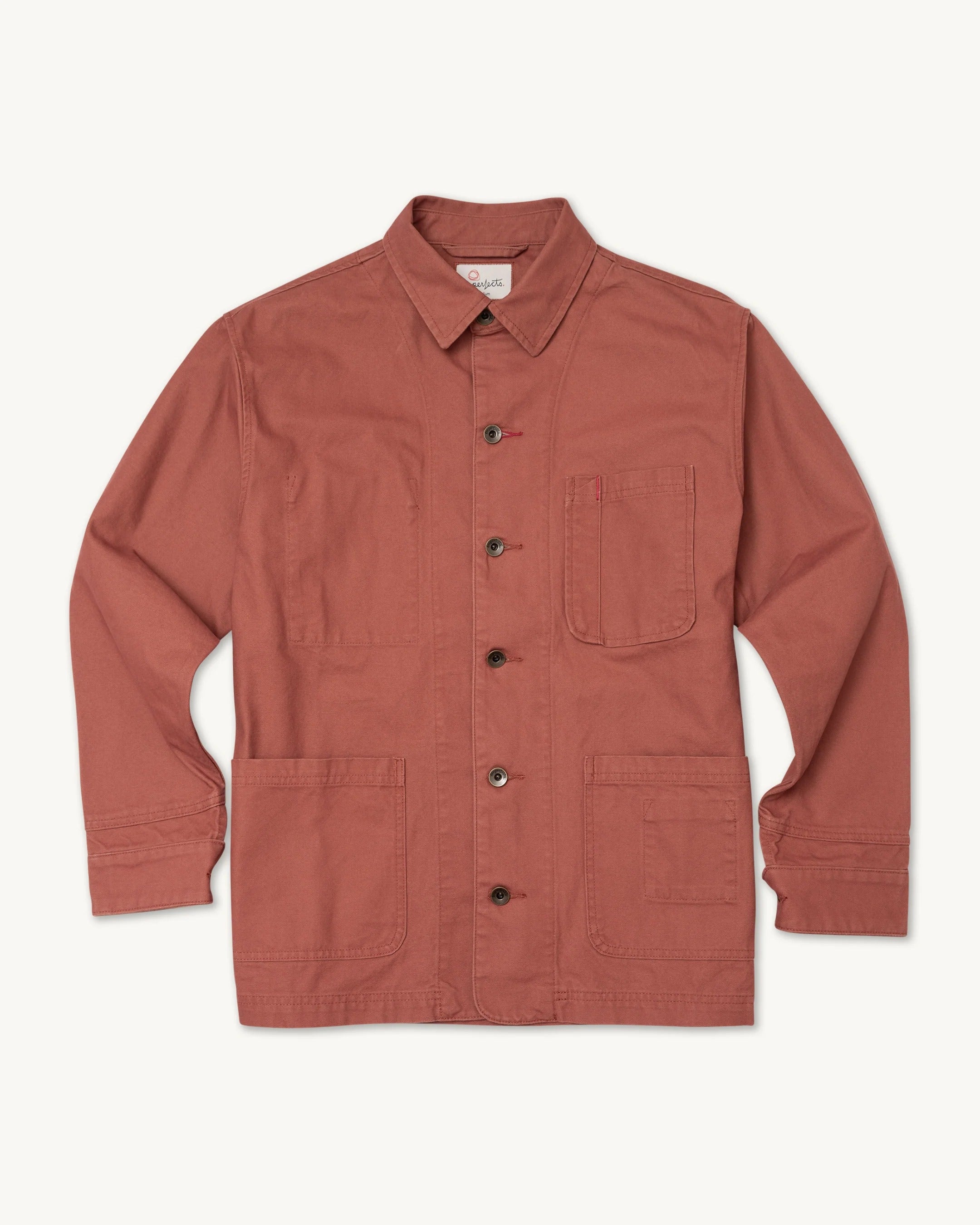 Imperfects Cunningham Coat in Craft Canvas / Oxide, a rust-colored button-up chore coat with a pointed collar, a single chest pocket, and two large utility pockets.