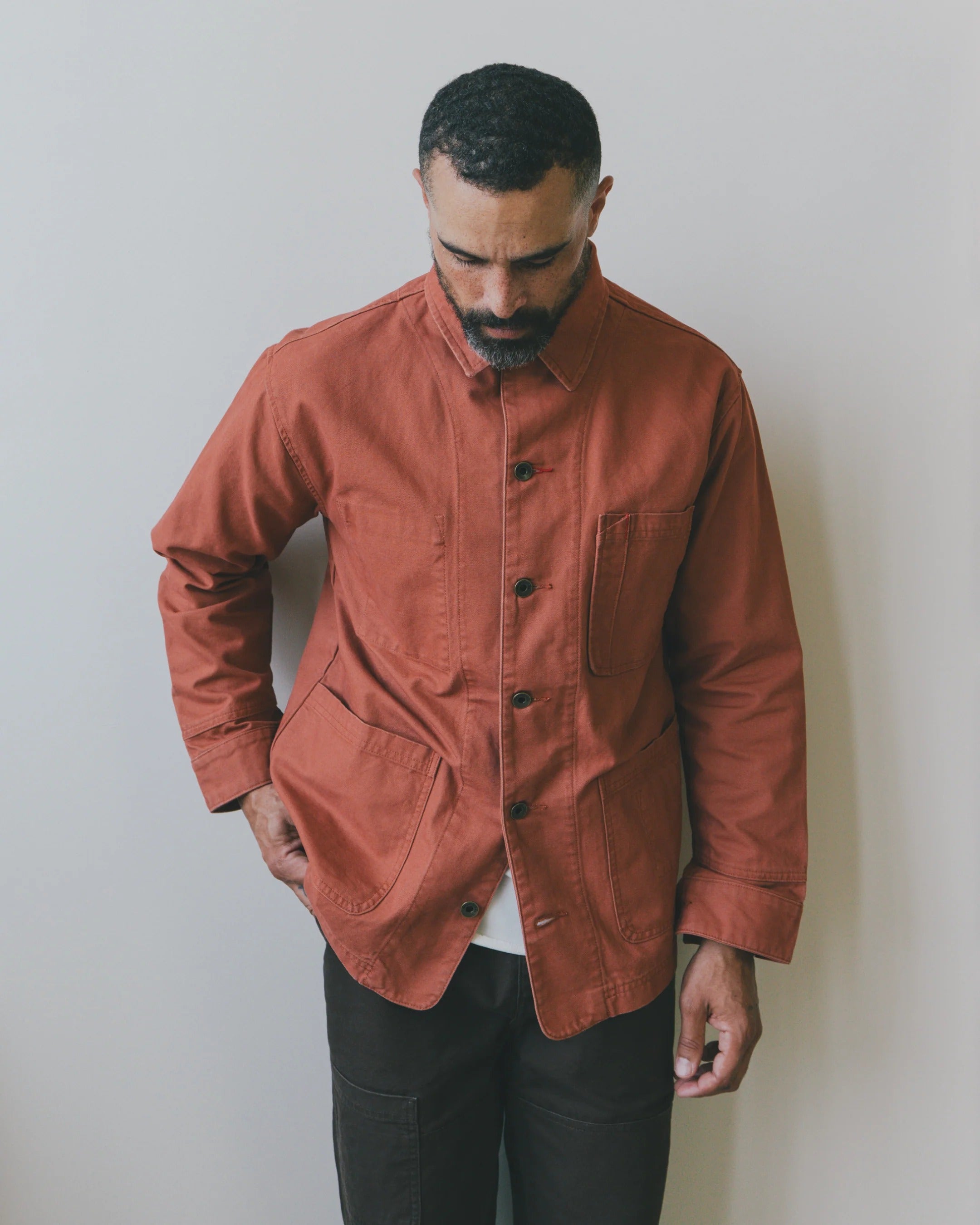 A man wearing an Imperfects Cunningham Coat in Craft Canvas / Oxide, a rust-colored canvas chore coat with large utility pockets.