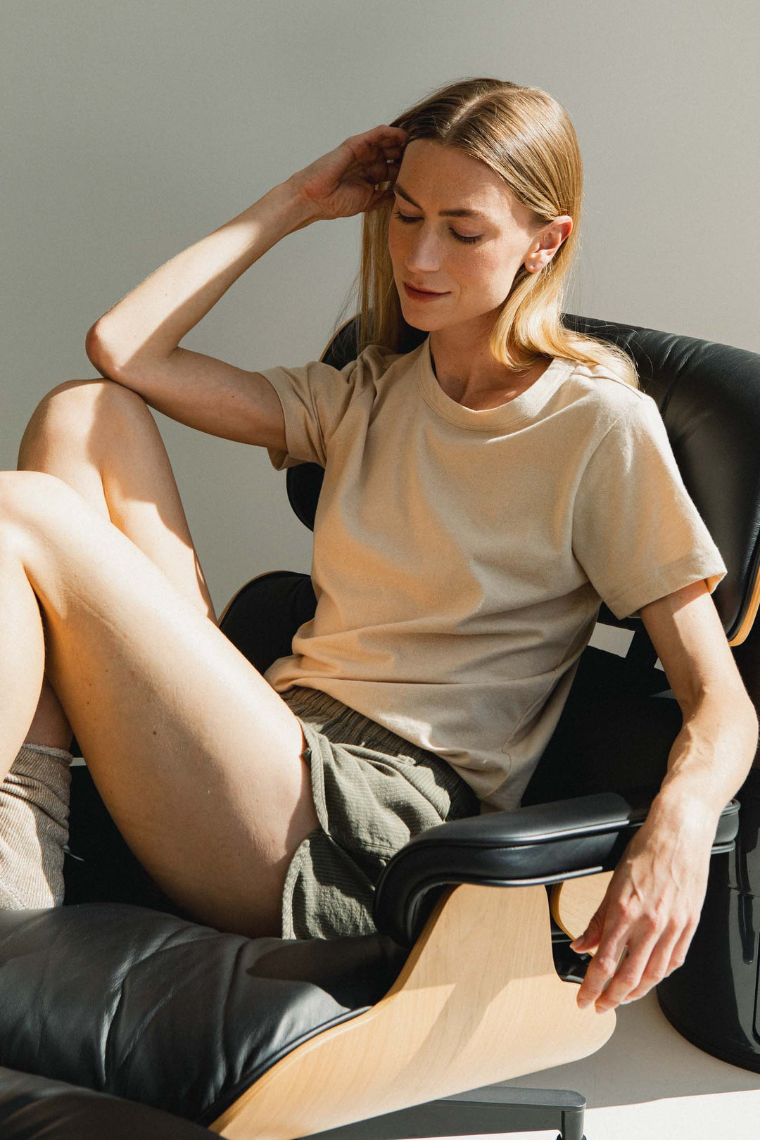 A person wearing a beige t-shirt and Bridge & Burn Luca Track Short / Olive Pinstripe sitting in a black leather lounge chair.