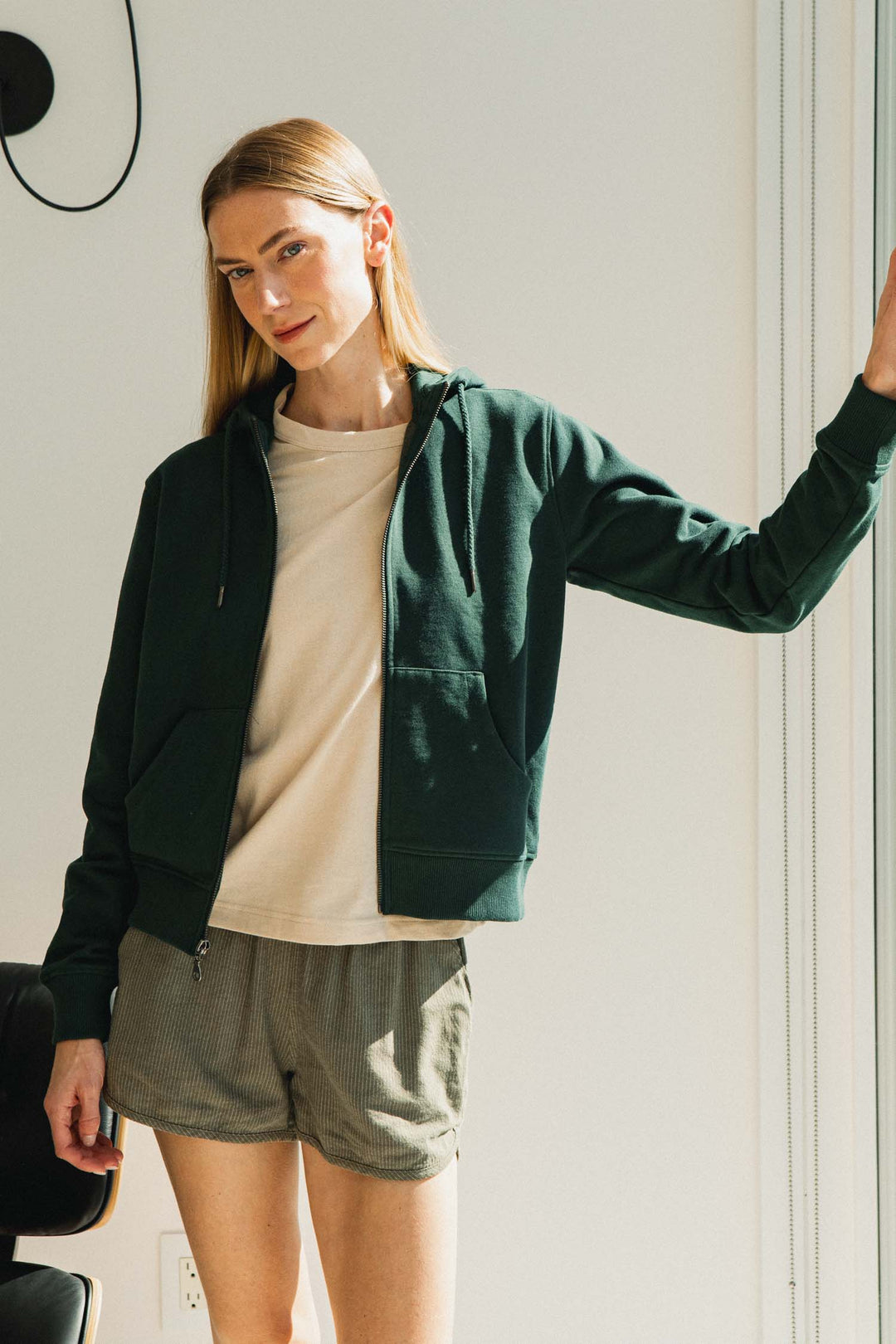 A person wears a dark green zip-up hoodie over a tan t-shirt and Bridge & Burn Luca Track Short / Olive Pinstripe.