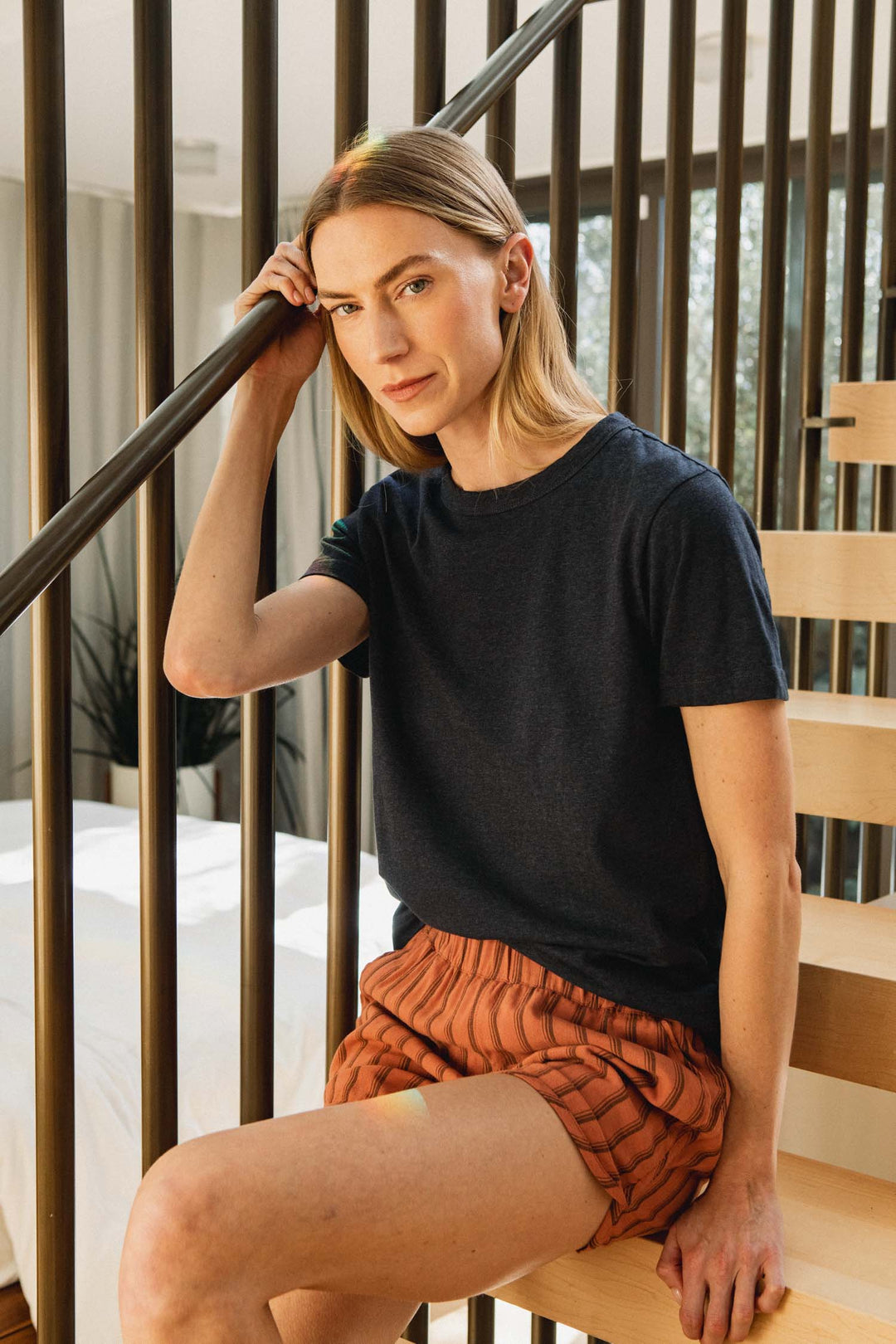 A person wearing a charcoal grey t-shirt and Luca Track Short / Rust Stripe sitting on a wooden staircase.