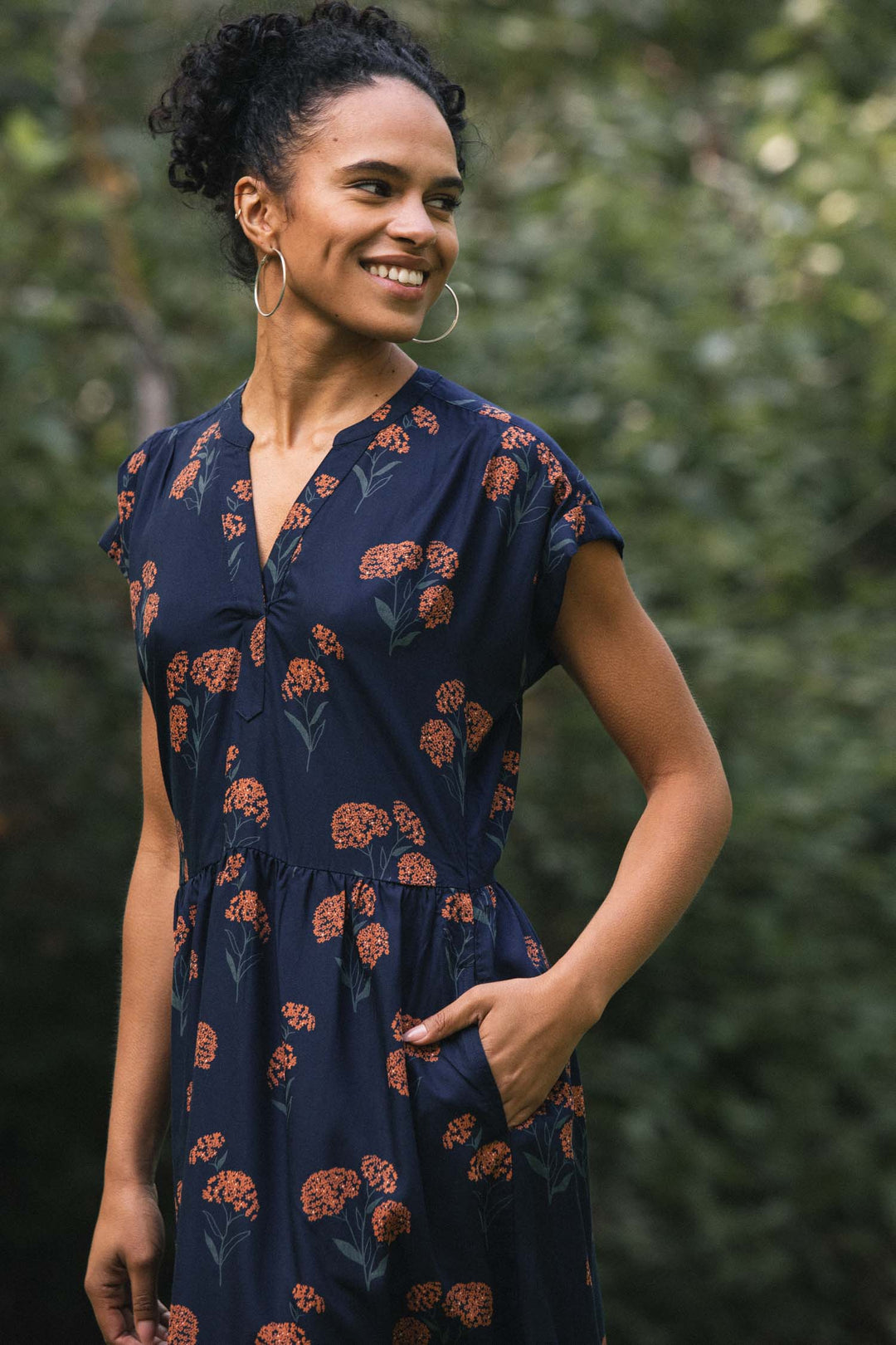 A person wearing the Bridge & Burn Ira Dress in Wildflower, a dark blue sustainable modal pullover dress with a short-sleeved cut, orange wildflower print, and side pockets.