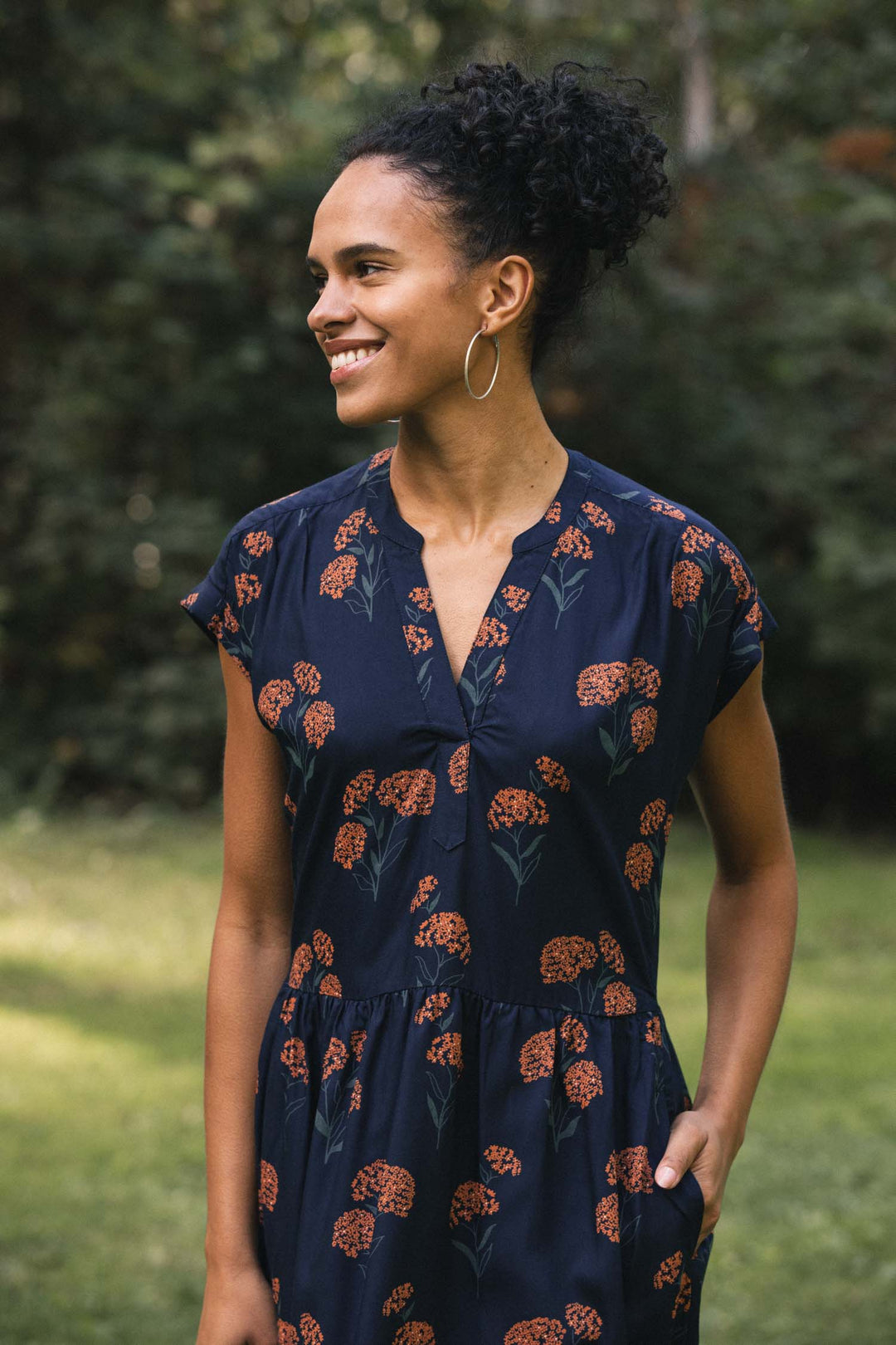 A woman wearing a navy blue V-neck Bridge & Burn Ira Dress / Wildflower with a wildflower print and short cap sleeves.