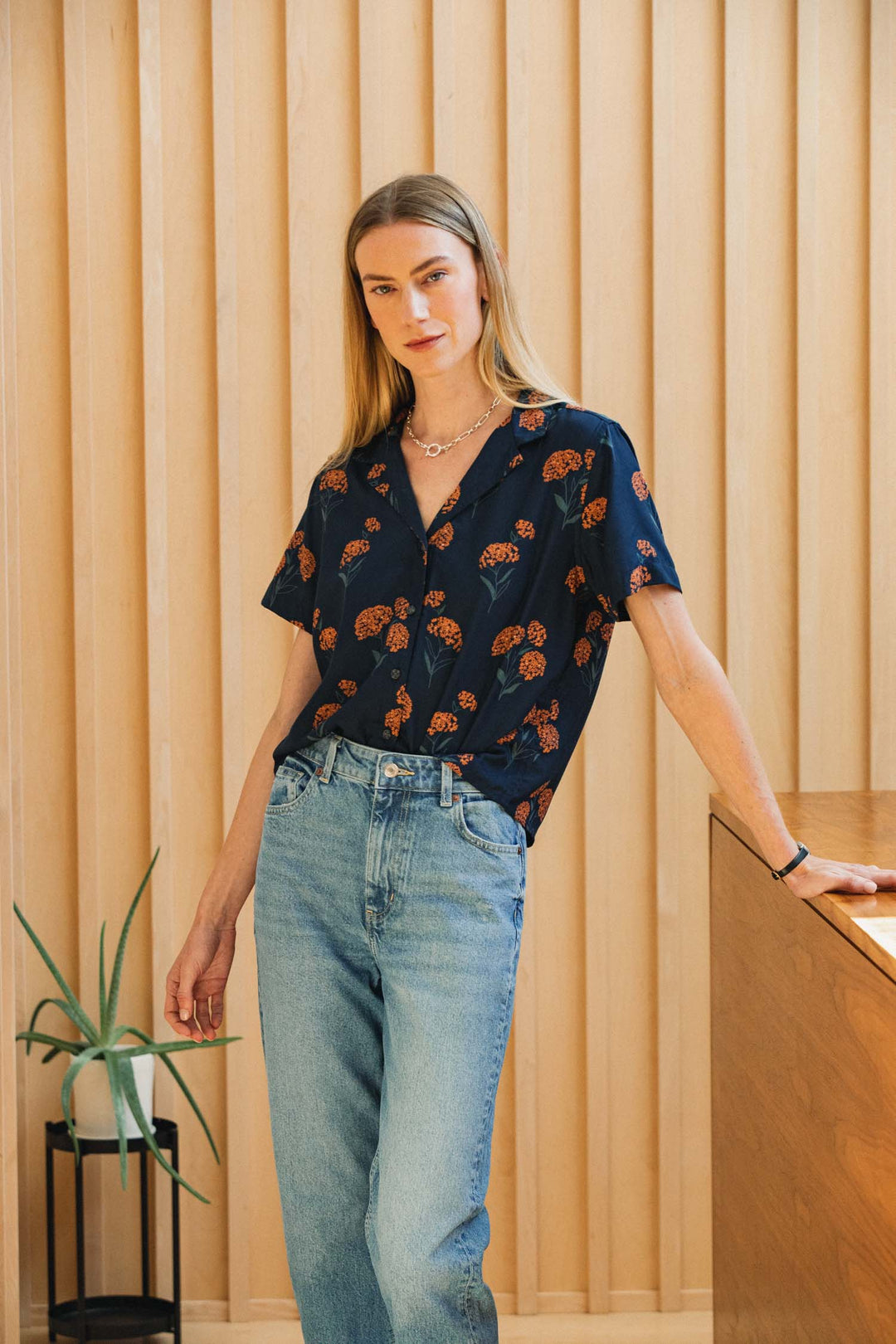 Woman wearing a Bridge & Burn Mila Cropped Shirt in Wildflower, a sustainable modal short-sleeve collared shirt with an orange wildflower print, paired with light wash jeans.