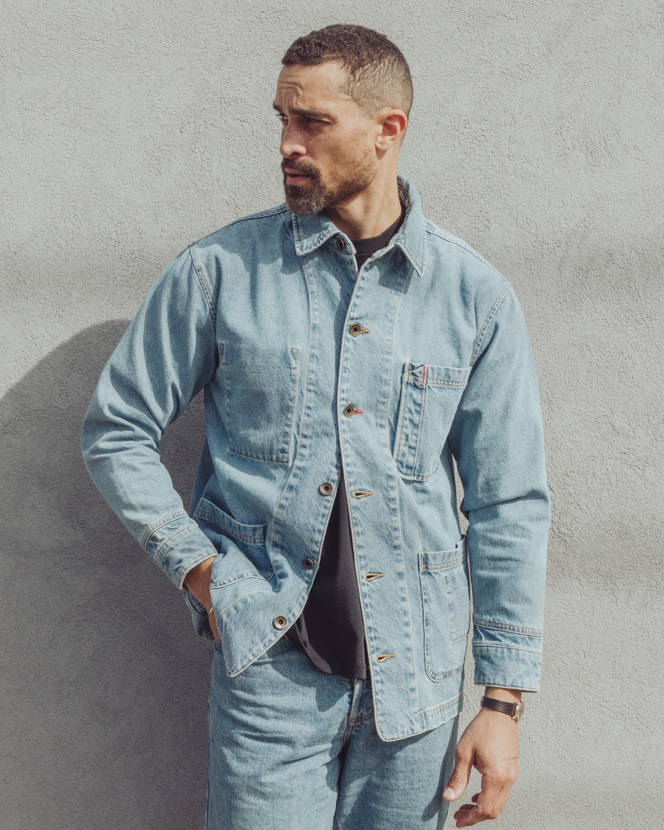 A man wearing an Imperfects Cunningham Coat in light-wash over a black shirt and matching Primo Denim jeans.