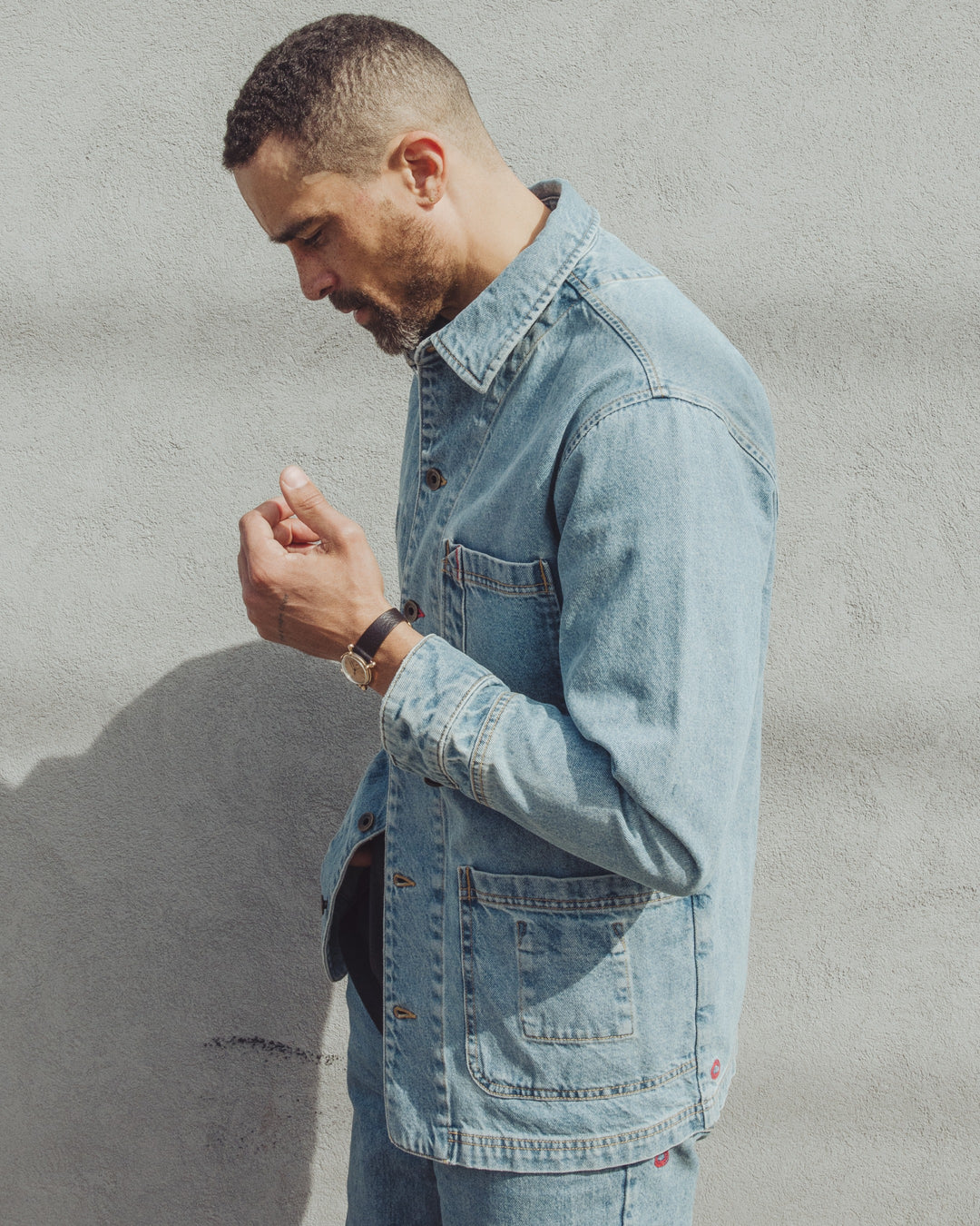 A man in profile wears an Imperfects - Cunningham Coat in light blue Primo Denim, featuring three patch pockets.