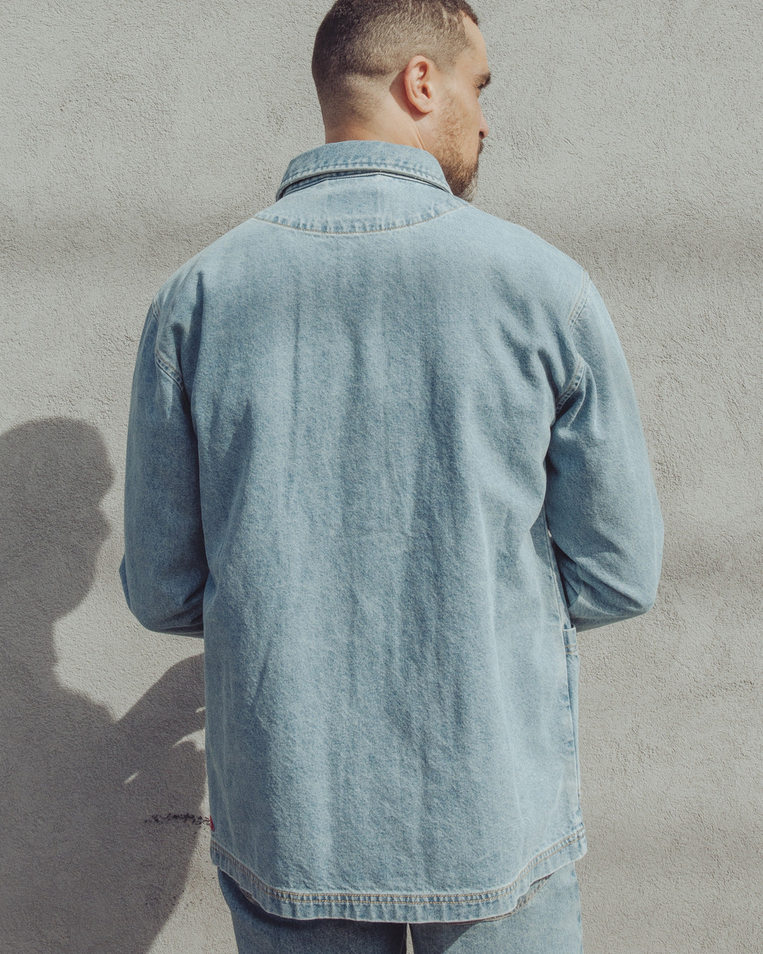 A man viewed from behind, wearing a light-wash Imperfects - Cunningham Coat / Primo Denim.