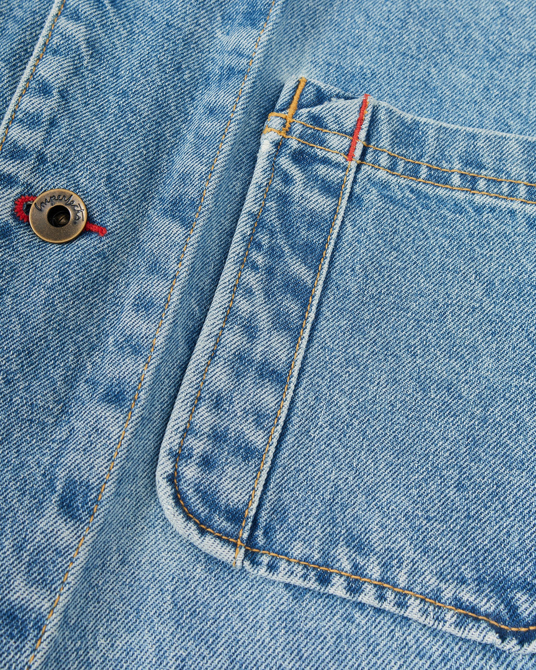 Close-up of the Imperfects - Cunningham Coat / Primo Denim in blue, featuring a large patch pocket, contrast stitching, and a metal button.
