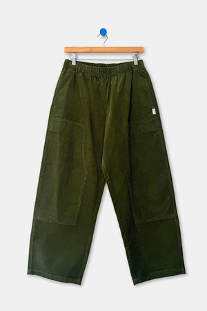 Le Bon Shoppe Gardener’s Pant in Bay Leaf corduroy, featuring an elastic waist and large patch pockets on the thighs, hanging on a wooden hanger.