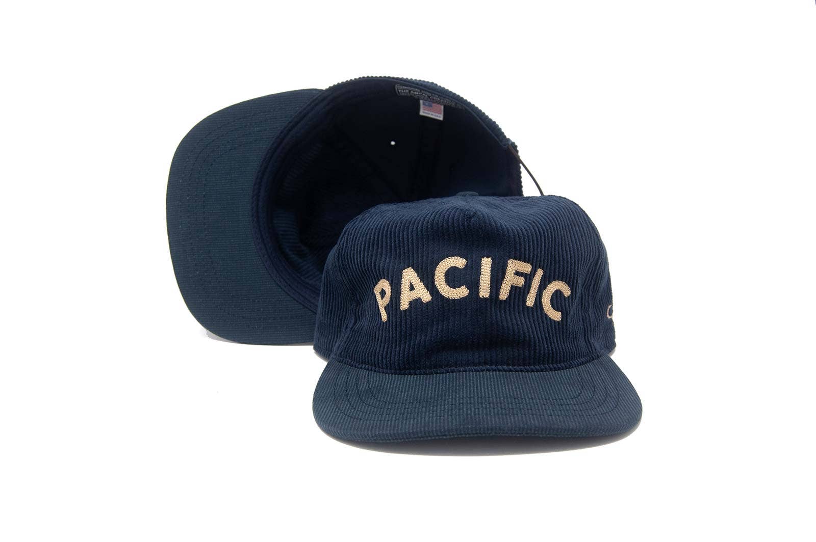 Two The Ampal Creative - Pacific III Strapback hats in navy corduroy with cream PACIFIC embroidery. One hat faces forward, the other is upside down to display the brim and interior—both set against a clean white background.
