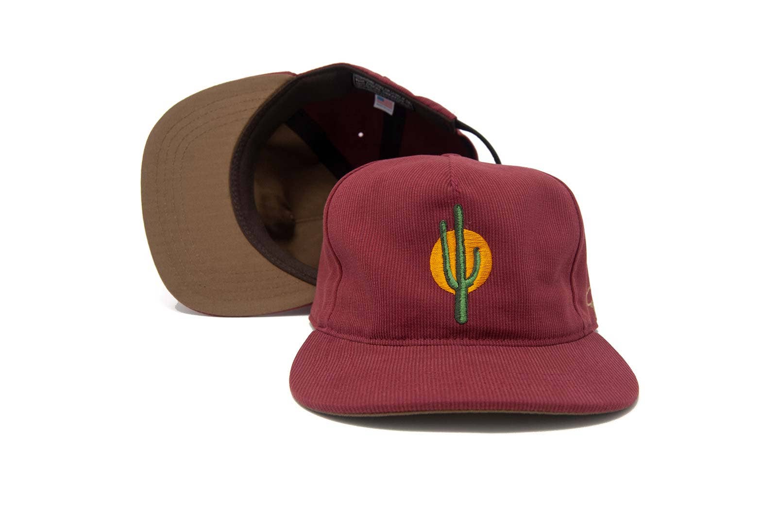 The Ampal Creative - Sunset Cactus / Brick is a cotton Bedford cloth hat made in LA, featuring a yellow sun and cactus embroidered on maroon. A second identical cap behind reveals the brown underside of the brim.