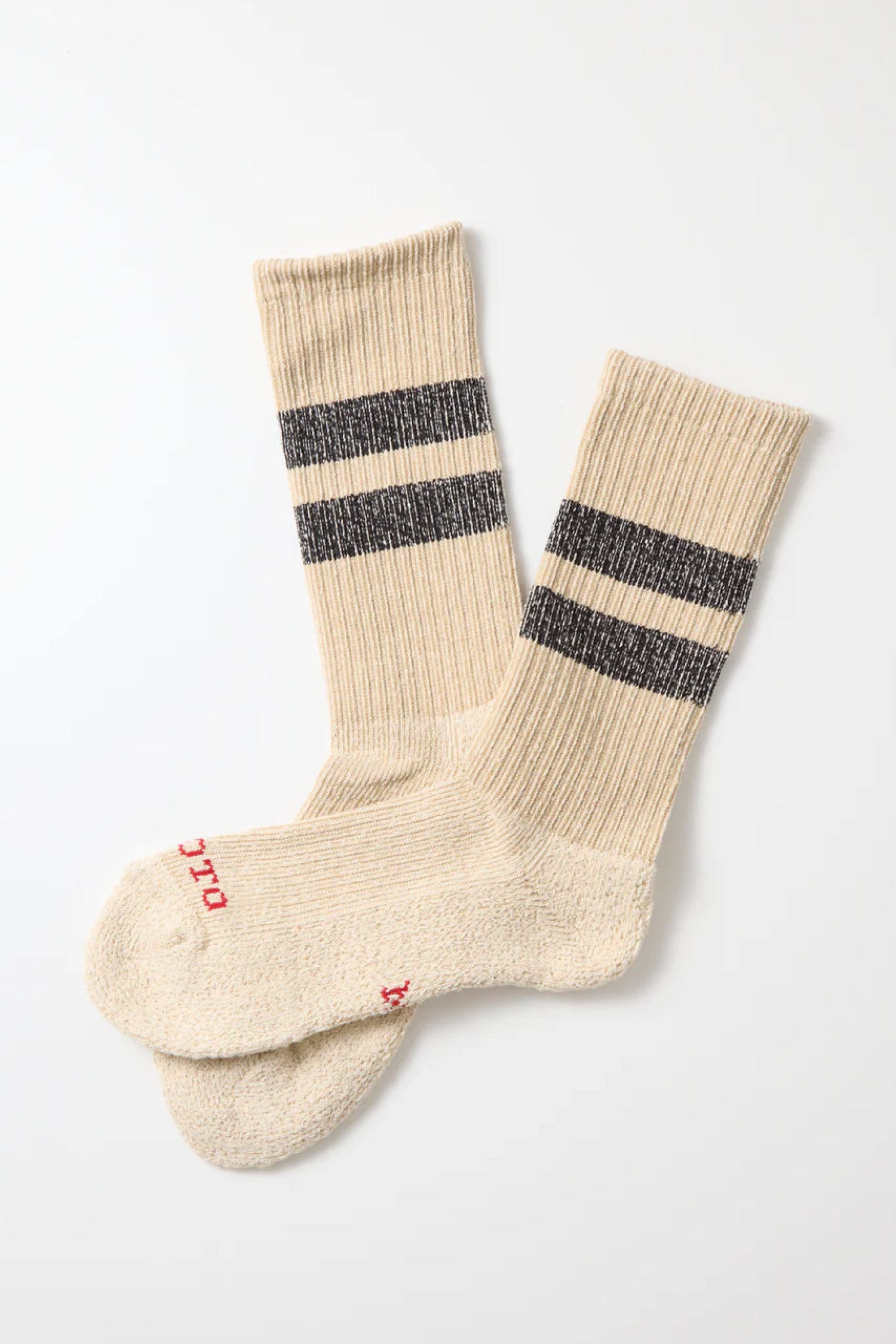 RoToTo Pile Stripe Marl Socks in Beige Black by RoToTo, made in Japan, feature beige ribbed fabric, two black stripes near the top, and small red text on the toes. Laid flat on a white surface.