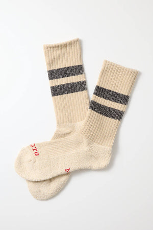 RoToTo Pile Stripe Marl Socks in Beige Black by RoToTo, made in Japan, feature beige ribbed fabric, two black stripes near the top, and small red text on the toes. Laid flat on a white surface.