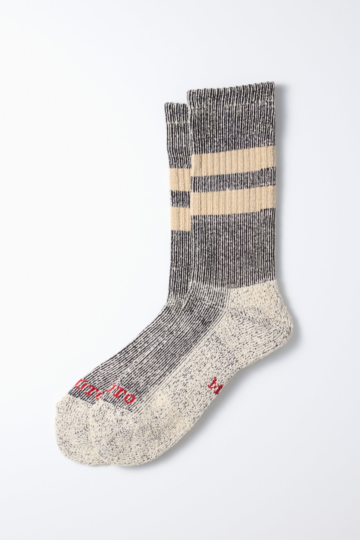 The RoToTo Pile Stripe Marl Socks in Black Beige are organic cotton socks by RoToTo, made in Japan with thick ribbing, two beige stripes near the top, and red text by the toe. Shown flat on a white background.