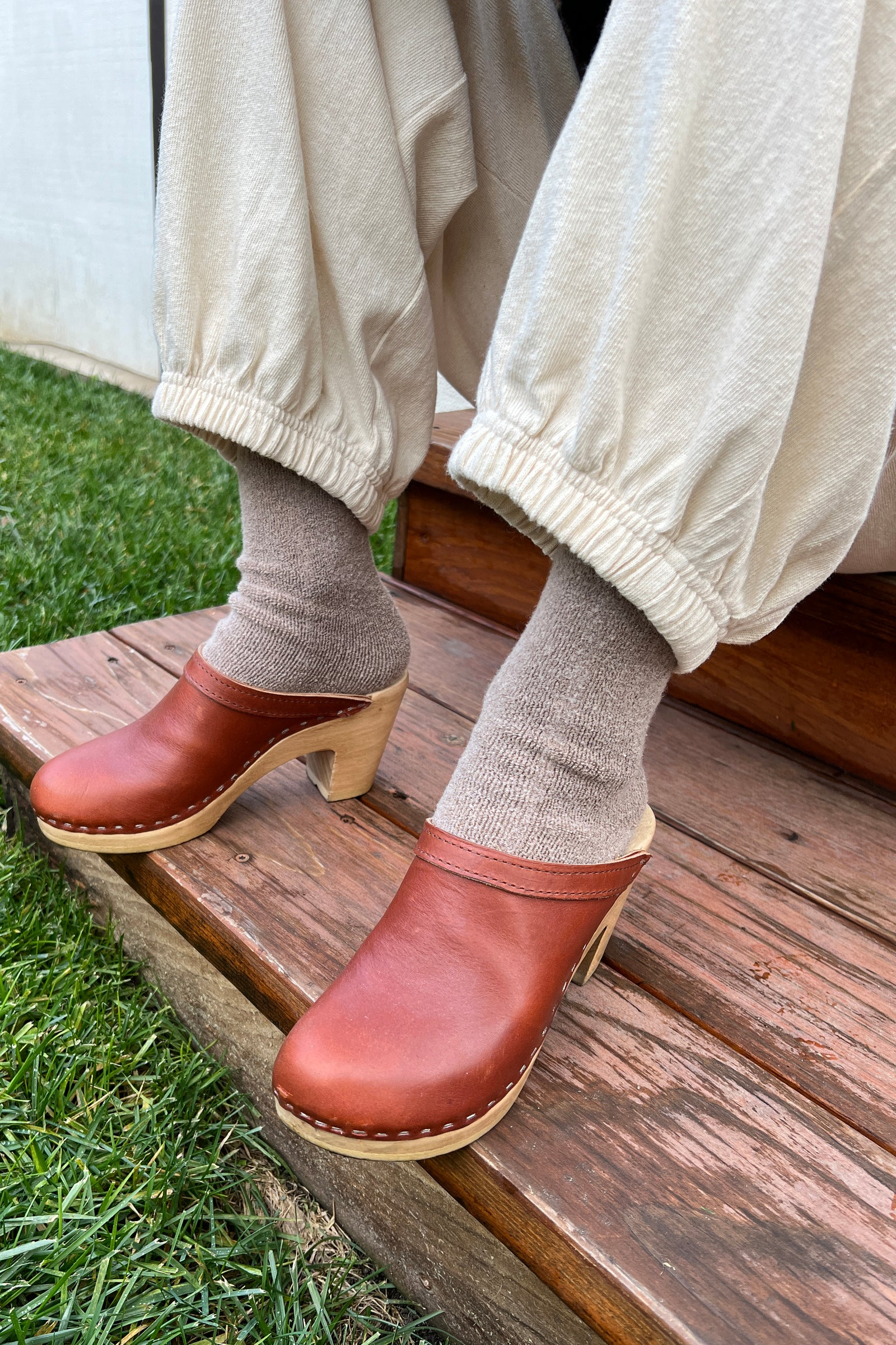 A person wearing Le Bon Shoppe - Balloon Pant / Natural stands on wooden steps next to green grass, paired with taupe socks and brown leather clogs.