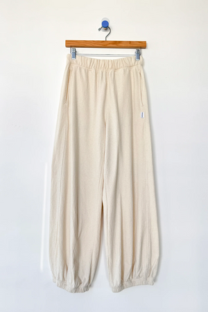 Le Bon Shoppe - Balloon Pant / Natural: Off-white, loose-fitting raw cotton pants with an elastic waistband and cuffs by Le Bon Shoppe, shown on a wooden hanger against a plain white wall.
