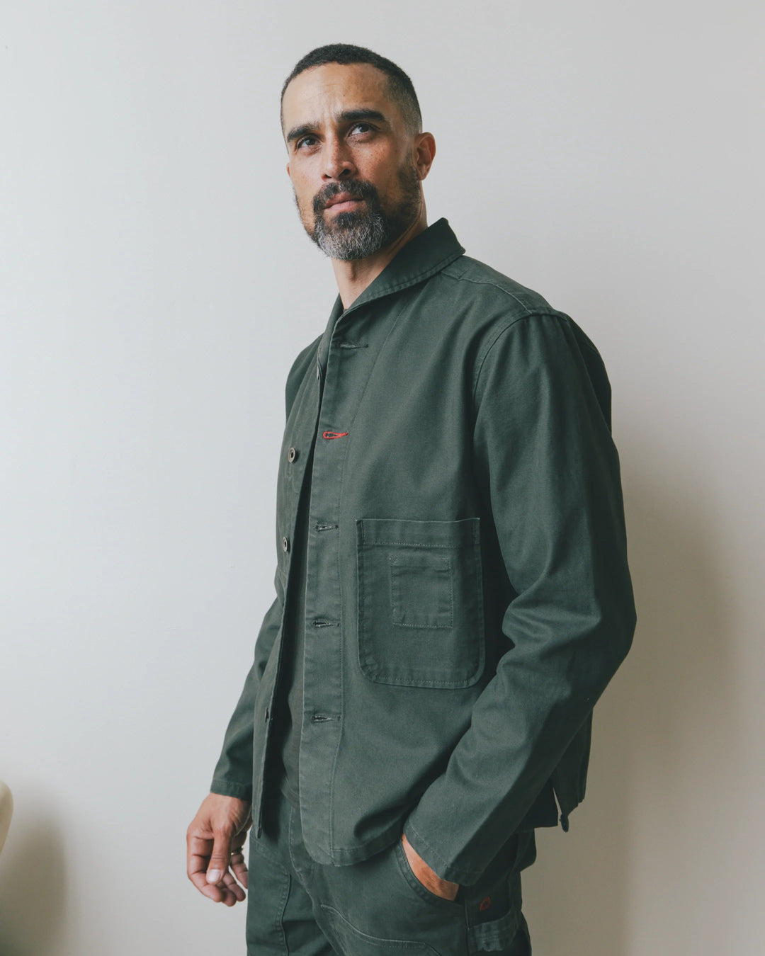 A man wearing an Imperfects - Shepherds Shirt Craft Canvas / Greenroom, a dark green organic cotton canvas overshirt with a collar, button-down front, and a chest pocket.
