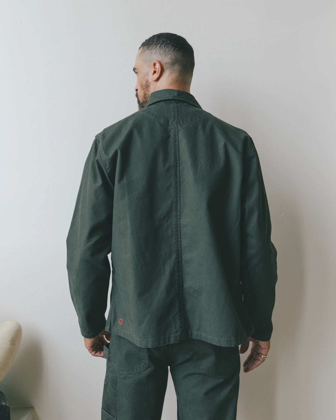 A man viewed from the back wearing an Imperfects - Shepherds Shirt Craft Canvas / Greenroom overshirt and matching trousers.
