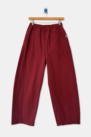 Le Bon Shoppe Arc Pant in Oxblood, featuring deep red high-waist wide-leg styling with an elastic waistband and side pockets, hanging on a wooden hanger.