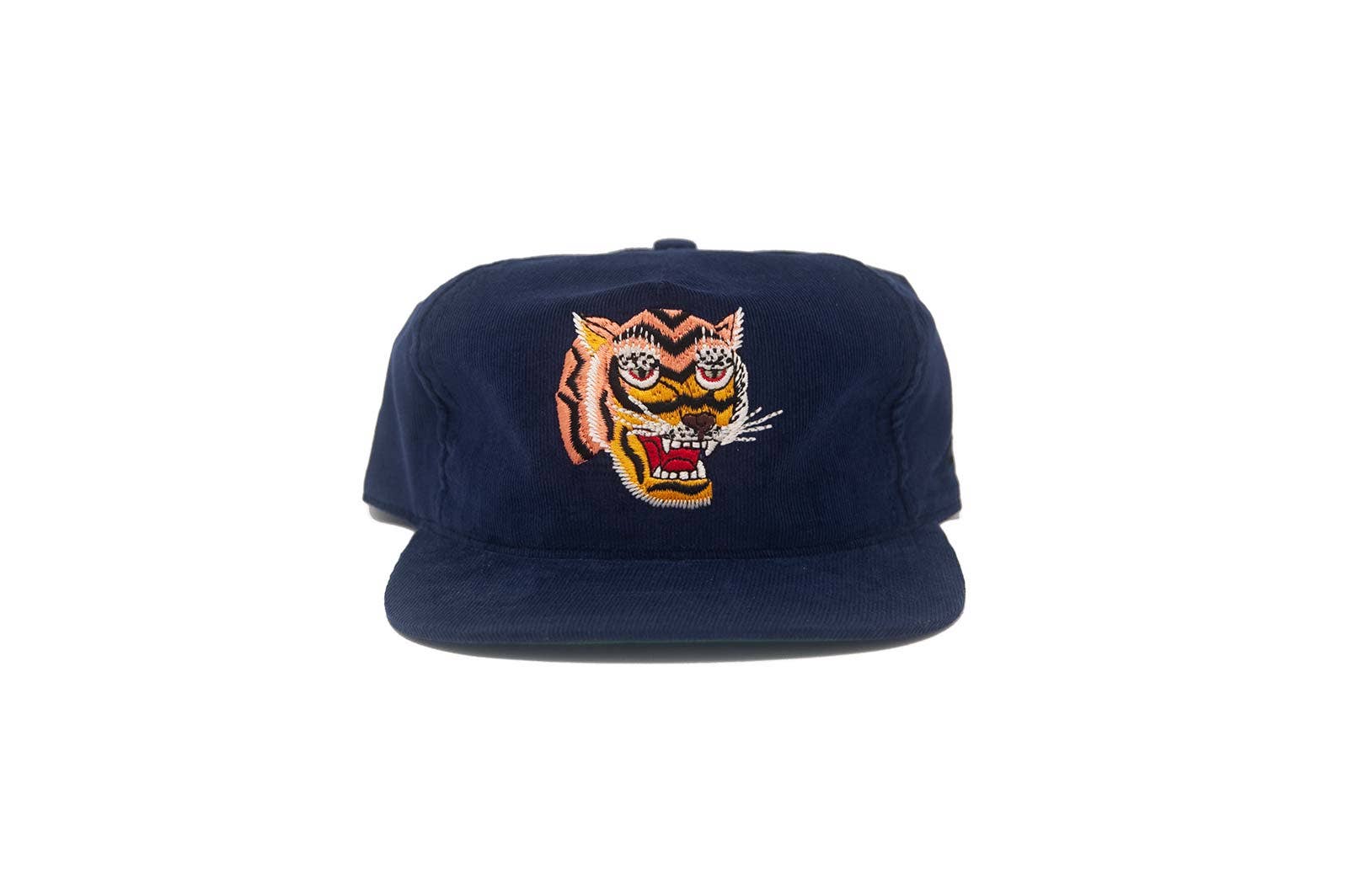 The Ampal Creative - Tiger III Snapback / Navy: a navy corduroy snapback baseball cap with an embroidered, colorful open-mouthed tiger head on the front, inspired by Vietnam-era Souvenir Jackets. Displayed on a plain white background.