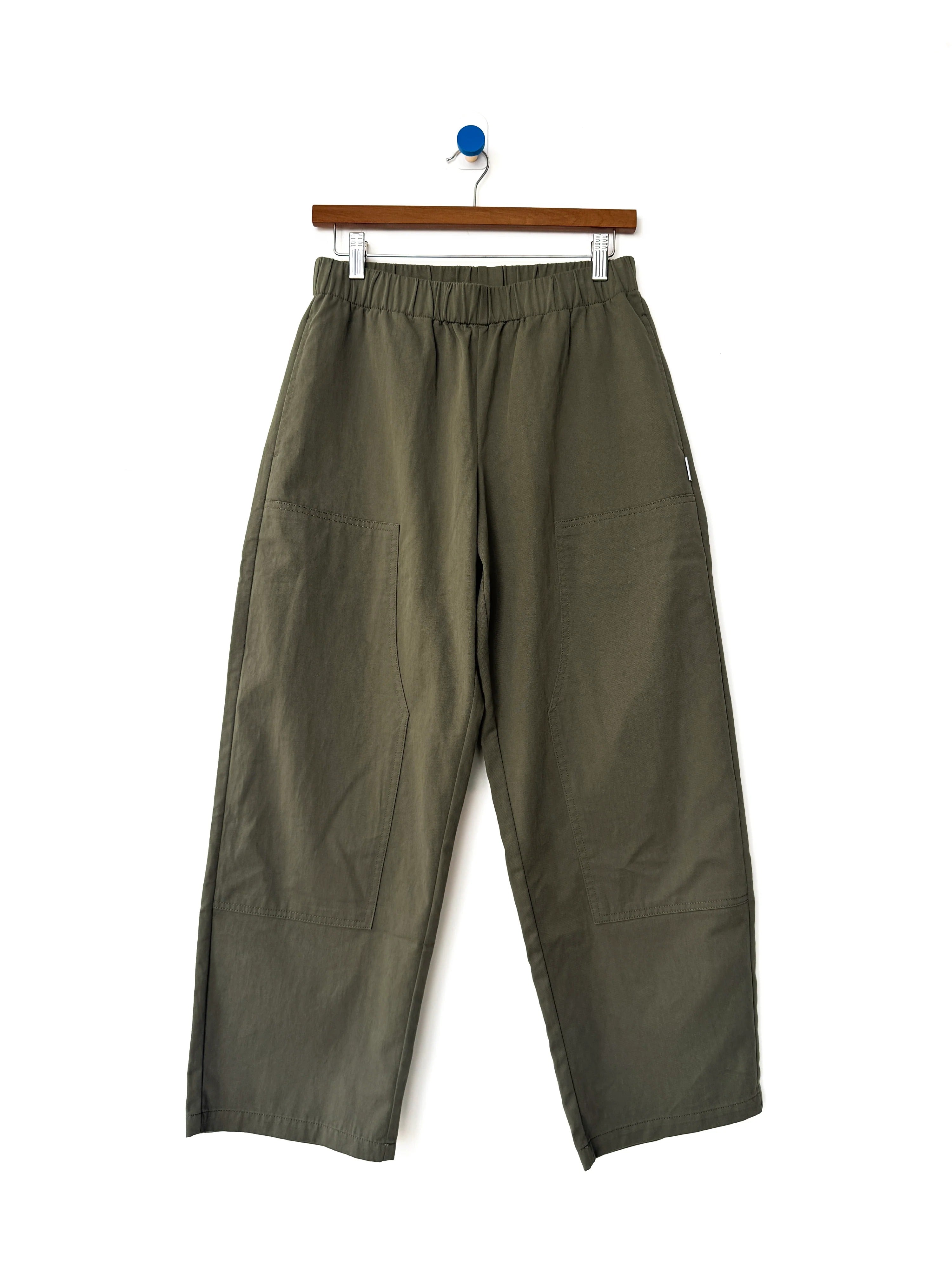 Le Bon Shoppe - Gardener’s Pant in Army Green, featuring a relaxed silhouette and spacious front pockets, crafted from lightweight cotton-nylon fabric, shown hanging on a wooden hanger against a white background.
