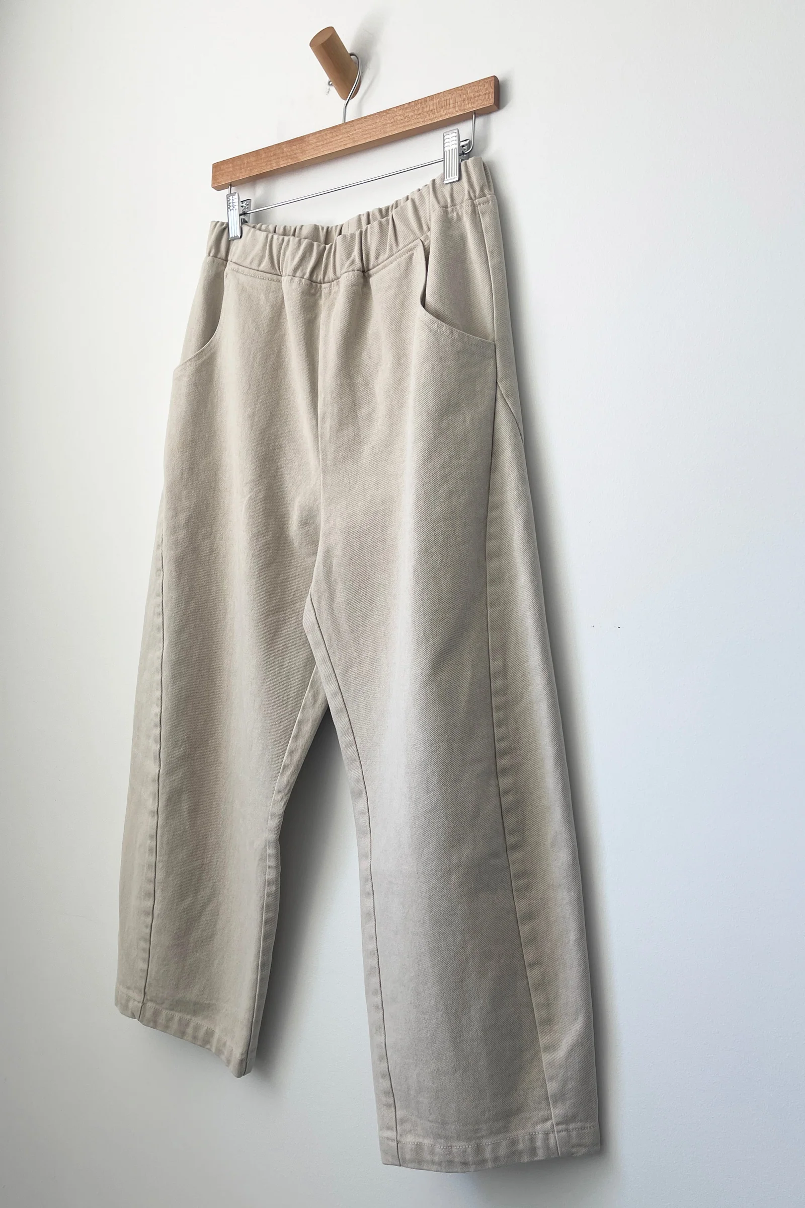 Le Bon Shoppe - Arc Pant / Natural: Heavy-weight canvas wide-leg pants with elastic waistband and side pockets, hangs on a wooden hanger against a plain white wall.